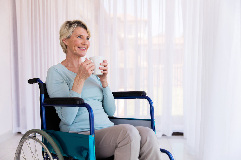Lady sitting in a wheelchair smiling and holding a cup of coffee